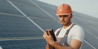 工程师在橙色头盔和棕色工作服检查阻力在户外太阳能电池板。印度男子在工位工作时使用万用表。检查太阳能电池板工作的人员