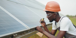 戴头盔，穿着工作服的技术员在户外用螺丝刀固定太阳能电池板。控制和维护太阳能电站的工作人员。穿制服的人用螺丝刀修理太阳能电池板