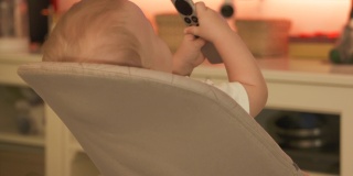白人小婴儿在家里看电视，可爱的小蹒跚学步的孩子拿着电视数字媒体播放器的遥控器。