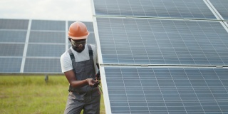 穿制服的技术员使用万用表检查太阳能电池板的电压。非裔美国人控制绿色能源的生产。穿着工作服的人在测量太阳能电池板的电阻
