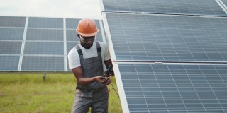 近距离拍摄的非裔美国人，穿着灰色工作服，在户外测量太阳能电池板的阻力。有能力的技术员在现场检查时使用万用表。用万用表测量电压