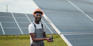 工程师在户外测量太阳能电池板的安培数。穿着灰色工作服的非洲人在户外测量太阳能电池板的阻力。有能力的技术员在现场检查时使用万用表