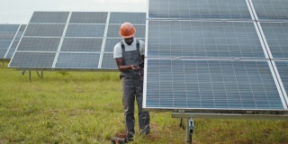 维护和替代能源。专业技术人员穿着工作服，使用万用表检查太阳能电池板的电压。非裔美国人控制绿色能源的生产