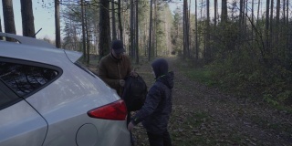 一位中年男子和他的儿子在森林里从汽车后备箱里取出背包