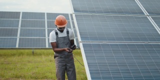 非裔美国人控制绿色能源的生产。穿着灰色工作服的人在户外测量太阳能电池板的电阻。人、维护和替代能源的概念