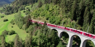 一列红色列车在瑞士阿尔卑斯山的Landwasser高架桥上行驶的鸟瞰图