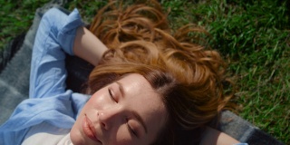 特写快乐的女孩躺在绿色的草地上。美丽的女人在户外享受阳光。