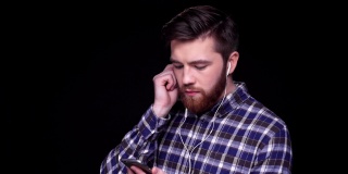 一个留着胡子的年轻人戴着耳机在手机上选歌