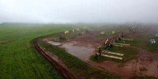 雨后雾蒙蒙的油田，从空中俯瞰油田油泵。泥泞的地面水坑，艰苦的工作条件。