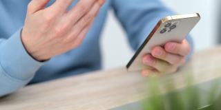 4 k。男子使用iPhone 12智能手机按手指，阅读社交媒体，打字或在线购物。在家里或工作时用双手拿手机。在俄罗斯圣彼得堡24.04.21号桌
