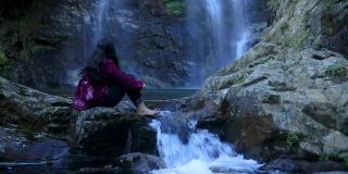 女孩坐在岩石上，瀑布从山上流动的水从平角森林