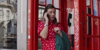 年轻开朗的女子在旧的红色电话亭里用智能手机聊天