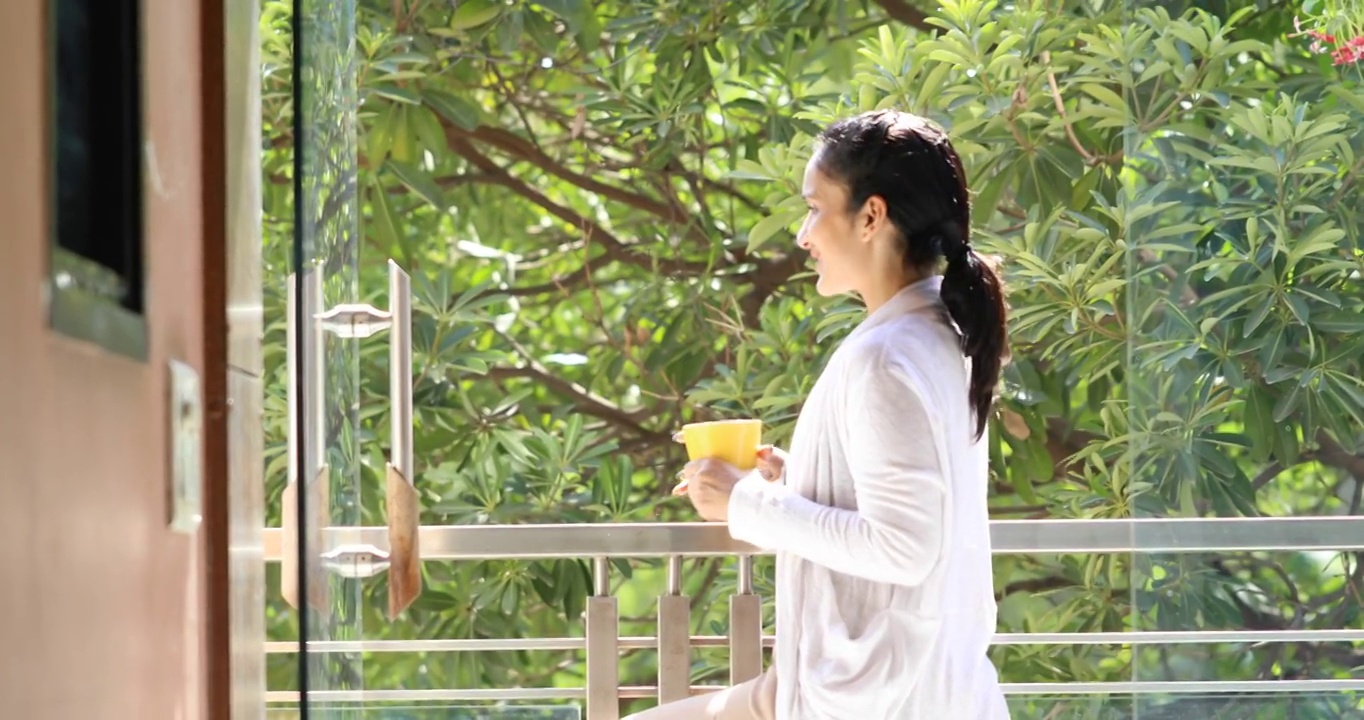 女人一边喝咖啡一边从阳台欣赏风景