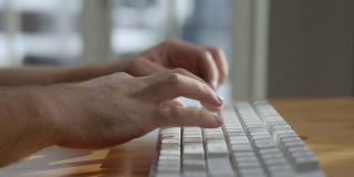 年轻男子学生在家里用电脑键盘打字。人在电脑上书写研究文件。盖伊在桌面键盘上工作的办公室。专业用户工作者客户支持