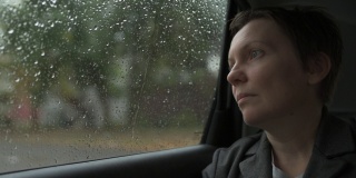 一个忧心忡忡的女商人，在雨中等在车里，望着窗外