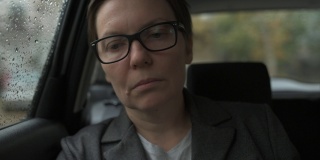 一个忧心忡忡的女商人，戴着眼镜，在雨中等在车里，望着窗外