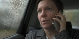 下雨的时候，严肃的女商人在车后座用手机聊天