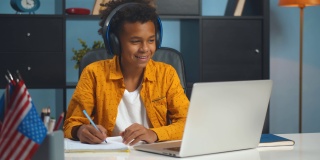 一个青春期前的非洲裔男生在家里用笔记本电脑做作业。