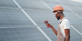 男性手持电子热成像仪近太阳电池户外的特写。非裔美国技术员控制站内光伏板温度