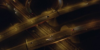夜间的高速公路上，无人机从上到下拍摄了经过桥梁和高架桥的十字路口的汽车。