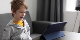 一个快乐的小男孩在家里玩着数码平板电脑。孩子们的自由时间、科技和互联网