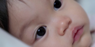 婴儿的特写:喝完奶瓶里的牛奶后，婴儿眨着眼睛微笑。孩子眨眼。娃娃脸开心的笑。亚洲的孩子。