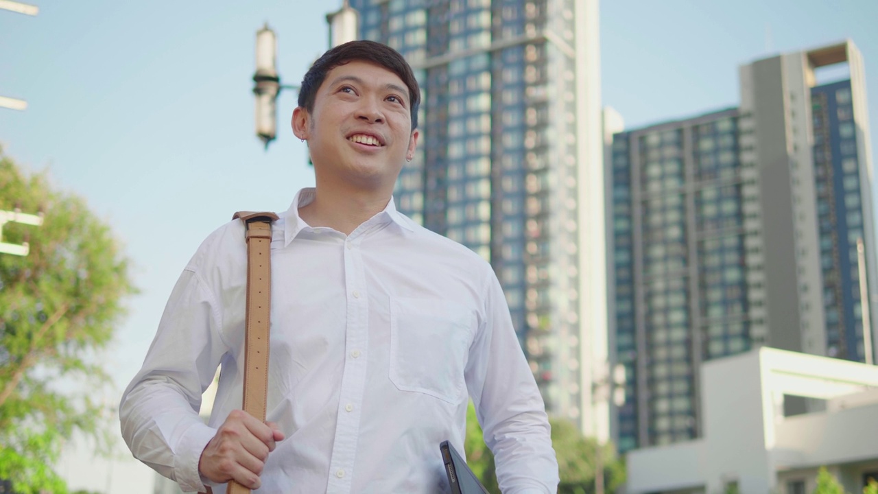 快乐的亚洲商人在现代城市的街道上行走的肖像