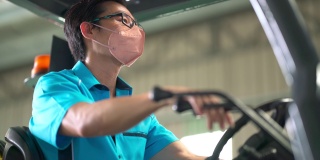 亚洲华人男性仓库工人，带着口罩在工业工厂操作叉车