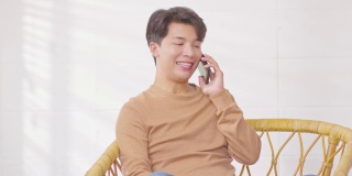 幸福英俊的亚洲年轻人微笑着和女朋友在家里用手机聊天。迷人迷人的少年拿着手机跟人聊天。偷拍