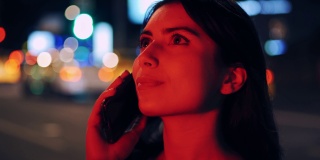 迷人的女人微笑时使用智能手机在街上。夜市灯光散景背景。慢动作