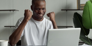 高兴兴奋的商人庆祝他的成功。获胜者是一个在办公室用笔记本电脑看新闻的黑人