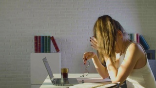 最后期限概念——厌倦了长时间使用电脑后，年轻女子摘下眼镜，擦鼻梁，减轻痛苦的感觉，休息，坐在工作场所视频素材模板下载
