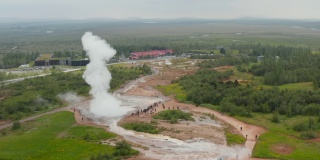 人们站在那里看着间歇泉喷出沸腾的水。自然地热活动的幻灯片和平盘照片。冰岛