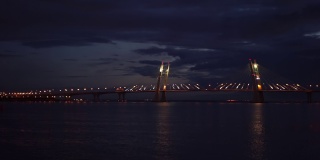 夜晚有灯光照亮的路的桥。镜头。大桥横跨城市岛屿之间的河流，飞鸟在镜框中飞翔，静观水面，平静如水