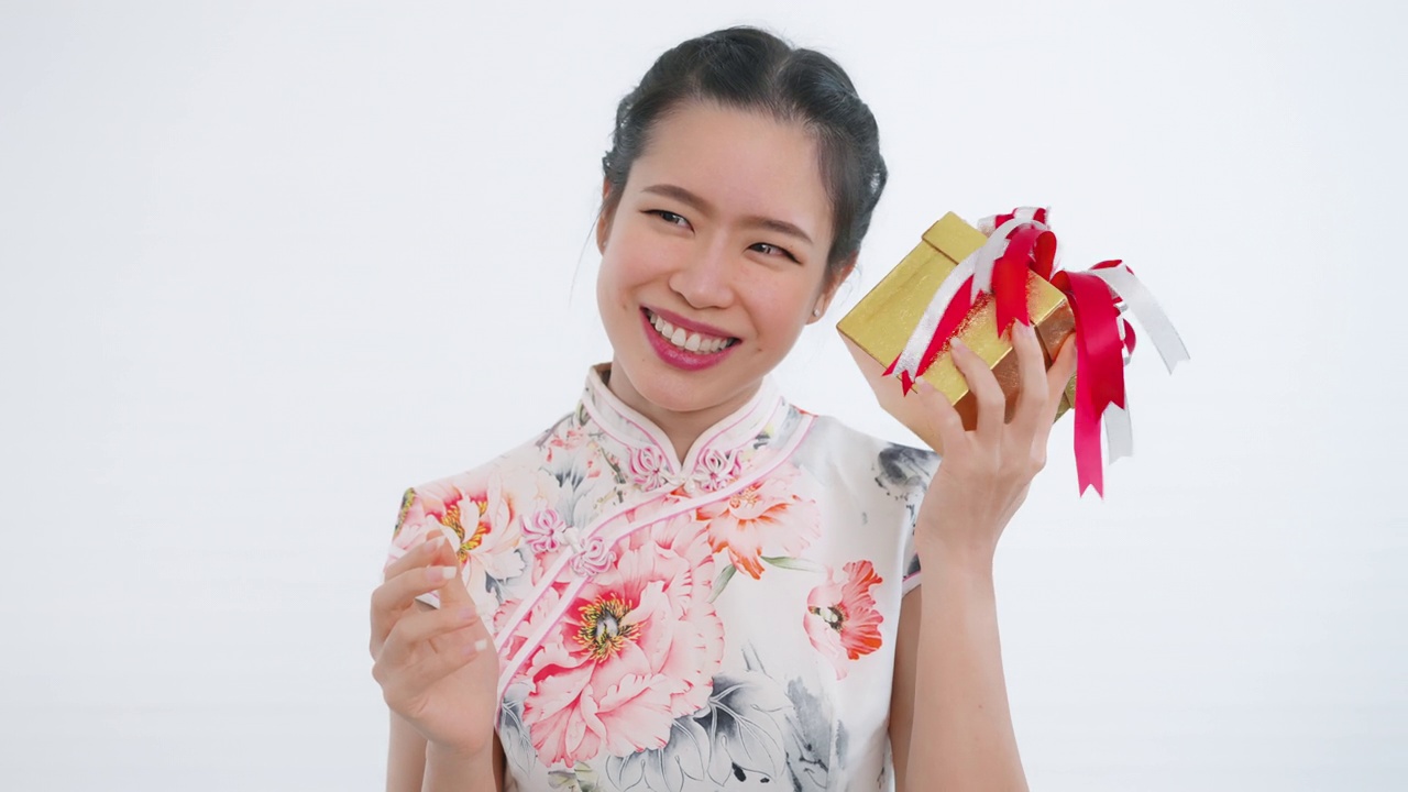 中国/亚洲妇女打开她手中的一个金色的大礼盒，她从她的家人，亲戚和朋友为新年的快乐，在中国的春节，穿着旗袍白色的衣服