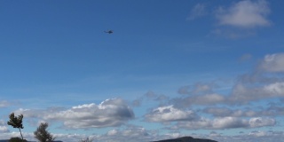 一架军用直升机在蓝天上飞行，天空中有蓬松的云朵和灰色