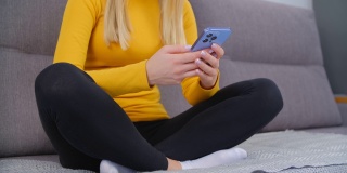 健康的年轻女子在智能手机上打字。女性使用手机app进行在线交流。禁闭在家时，坐在沙发上用现代手机发送信息的人