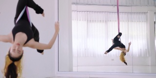 快乐迷人的年轻亚洲女运动员做反重力瑜伽练习，练习在空中吊床倒置的姿势。年轻漂亮的妇女穿着黑色运动服，在空中瑜伽的变化Chakrasana，桥式。