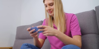 兴奋的白人女性在家里用现代智能手机玩手机游戏。快乐的年轻成年女性坐在沙发上用时髦的手机设备玩视频游戏，脸上带着愉快的微笑