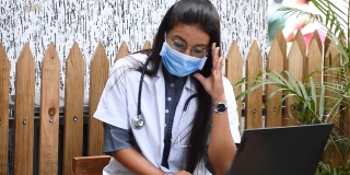印度女医生坐在笔记本电脑前。在医院工作的压力性头痛，由于印度冠状病毒病例的增加而感到压力。劳累过度的医生。