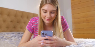 漂亮的白人女性在卧室里用手机应用程序打字。美丽的年轻成年白人女性在近距离4l视频与现代智能手机和社交媒体应用程序在线交流