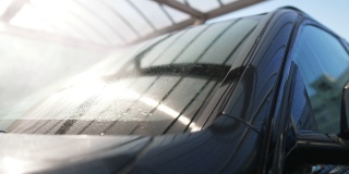 在阳光明媚的户外，高压水喷洒在汽车挡风玻璃上。洗车服务在阳光明媚的春夏季的一天。汽车维修的概念。