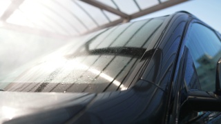 在阳光明媚的户外，高压水喷洒在汽车挡风玻璃上。洗车服务在阳光明媚的春夏季的一天。汽车维修的概念。视频素材模板下载