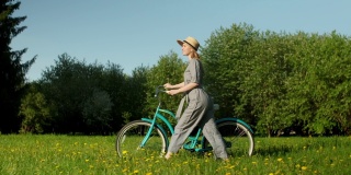 骑自行车的女人行走在乡村道路在夏天的时间。美丽的女人骑自行车戴着帽子在地上的道路绿色的草地有乐趣和享受生活