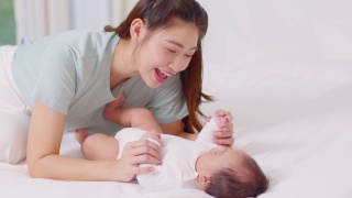 新亚洲妈妈玩可爱的新生婴儿在床上微笑和幸福在家里。妈妈和婴儿说话，牵着她的手一起笑。婴儿和母亲节的概念视频素材模板下载