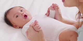 新亚洲妈妈玩可爱的新生婴儿在床上微笑和幸福在家里。妈妈和婴儿说话，牵着她的手一起笑。婴儿和母亲节的概念