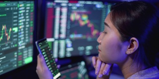 年轻的女商人使用多个电脑屏幕学习和交易加密货币和股票市场和交易所，同时工作到深夜