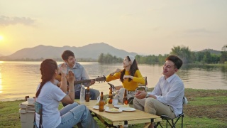 小组四人朋友亚洲男女野营，喝啤酒，庆祝，唱歌，弹吉他，玩乐，享受地面帐篷。日落假期期间的水库区域。视频素材模板下载