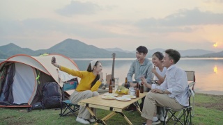 小组四人朋友亚洲男人和女人野营野餐庆祝，通过智能手机自拍享受乐趣和地面帐篷。日落假期期间的水库区域。视频素材模板下载