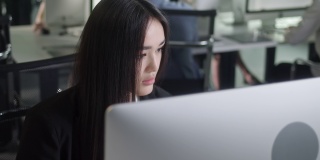 有吸引力的年轻女子在台式电脑上工作，而在大的开放空间办公室工作。正面商业女性的肖像看着室内的电脑屏幕